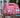A pink chunky knit handbag decorated with iridescent circular sequins, held up by a hand on a wooden deck.