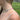 A close-up lifestyle shot of a model wearing a delicate, iridescent rainbow gradient beaded necklace with a blurred green outdoor background.