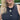 A woman with blonde hair wearing a black sleeveless top and a black beaded tassel necklace with a colorful frog pendant, s