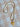 A gold chain necklace with clear rhinestones and a yellow and gold heart-shaped pendant featuring a clear heart-shaped gemstone, displayed on a beige and white checkered fabric background.