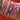 A close-up of a person's wrist wearing a stack of multiple beaded bracelets in pink and gold, set against a solid orange background.