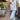 A woman wearing a white 3D floral top, light wash jeans, and a dusty pink fringed bag standing on an outdoor patio.