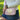 A woman outdoors wearing a cream ribbed knit cardigan and denim skirt, carrying a light pink crossbody bag with a cream heart-shaped patch on the front.