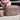 A pink faux-leather crossbody bag with a large beige heart on the front, displayed alongside a pink beaded necklace on a pink mannequin bust and a pink and white beaded bracelet on a burlap pillow, all set on a beige and white checkered tablecloth.