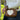A woman outdoors wearing a white ribbed knit sweater and dark jeans, carrying a brown crossbody bag with a large white heart on the front.