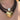 A close-up of a multi-strand necklace worn on a person's chest. The necklace features dark brown beaded strands, a single lustrous pearl bead, and a hammered gold heart-shaped pendant.