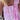A woman wearing a pink tie-dye sleeveless top with a ruffled shoulder and a long colorful beaded necklace