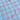 A beaded necklace with alternating pink and white striped beads, accented by a small white heart-shaped bead and gold-tone hardware, laid flat on a blue and white checkered fabric background.