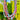 A set of colorful beaded necklaces hanging outdoors in front of green trees and shrubs. The necklaces feature pastel pink, turquoise, white, and rainbow-striped strands with small white heart-shaped beads at the ends.